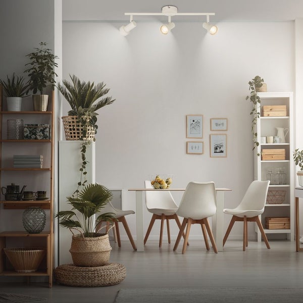Helles Esszimmer mit weißer dreiflammiger Deckenleuchte, Esstisch und vier weißen Stühlen im skandinavischen Stil. Dekoriert mit Pflanzen und Regalen.