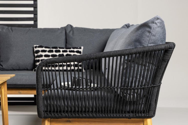 Detailansicht eines Lounge-Ecksofas mit schwarzer Seilbespannung, grauen Kissen, einem gemusterten Zierkissen und einem Holzgestell.