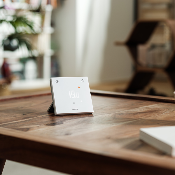 Ein Netatmo Smartes Thermostat steht auf einem hölzernen Couchtisch in einem Wohnraum.