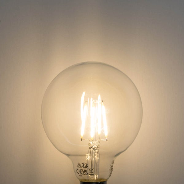 Eingeschaltetes LED-Filament-Leuchtmittel in Globeform aus Klarglas mit warmweißem Licht.