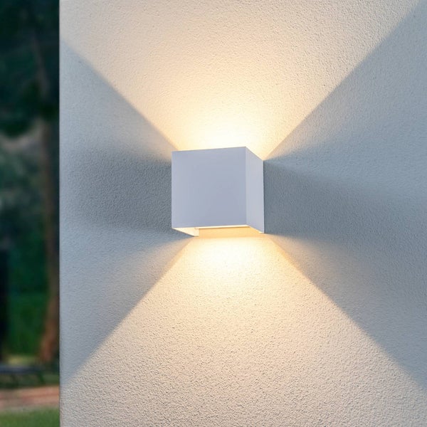 Moderne würfelförmige Außenwandleuchte mit Lichtaustritt nach oben und unten an einer strukturierten Hauswand.