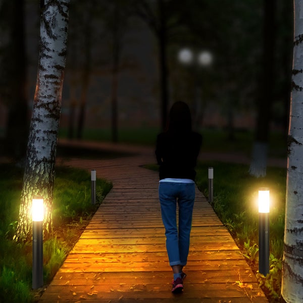 Eine Person geht auf einem von Gartenleuchten beleuchteten Holzweg entlang.