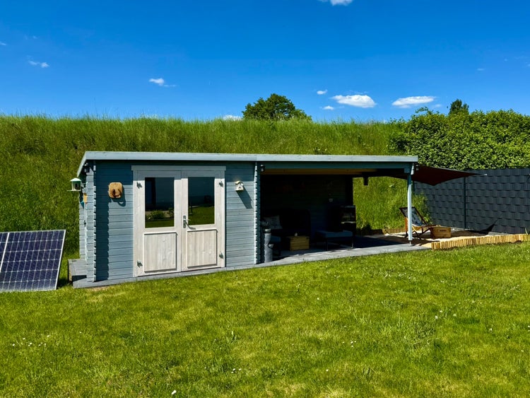 Modernes Gartenhaus aus Holz mit Flachdach, Doppeltür und überdachter Terrasse in einem hellen, weitläufigen Garten mit Rasenfläche.