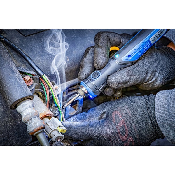 Akku-Lötkolben bei der Reparatur von Kabeln, Person mit Arbeitshandschuhen lötet Drähte, Rauch steigt auf.