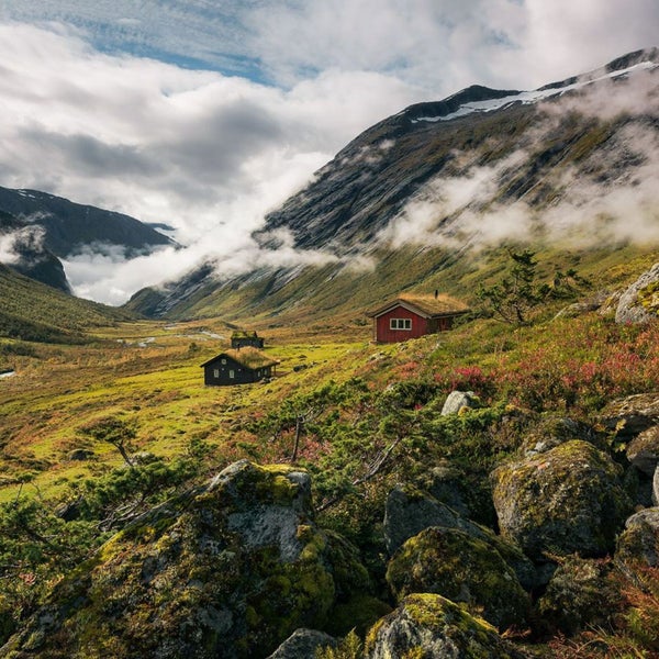 Landschaft mit Bergen, Wiesen und Hütten mit Grasdächern.