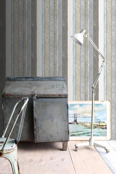 Raumansicht mit Tapete in Holzoptik, Metalltruhe, Stehlampe und Stuhl