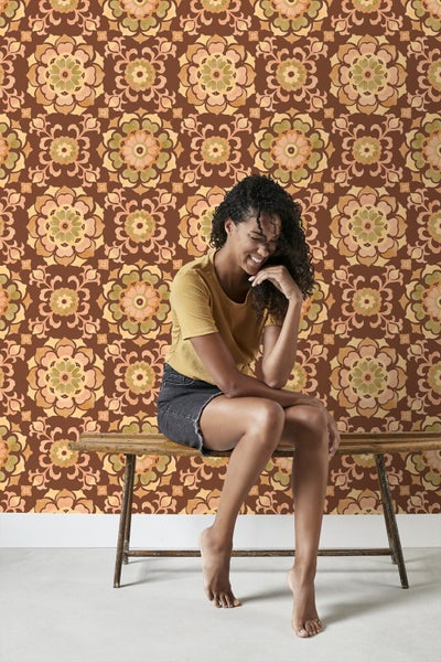 Frau sitzt vor einer Wand mit floraler Tapete auf einer Holzbank