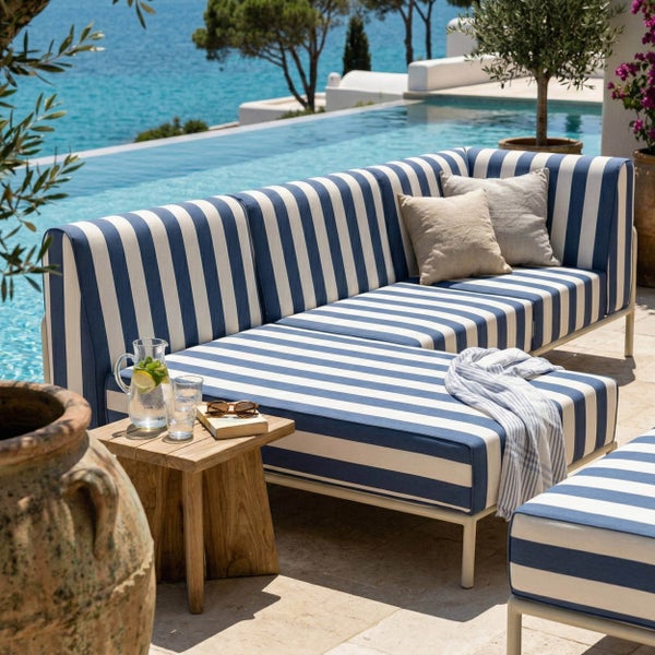 Gestreiftes Gartensofa und Hocker in Blau und Weiß auf einer hellen Terrasse am Pool mit einem Beistelltisch aus Holz.
