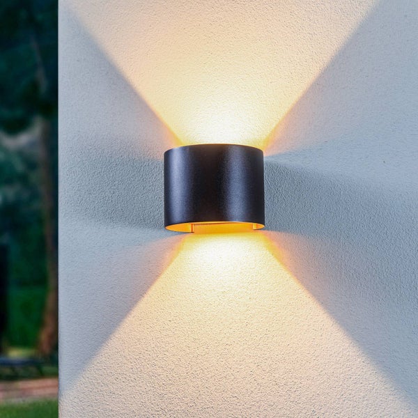 Moderne zylindrische LED Außenwandleuchte in Schwarz mit Lichtaustritt nach oben und unten an einer strukturierten Fassade.