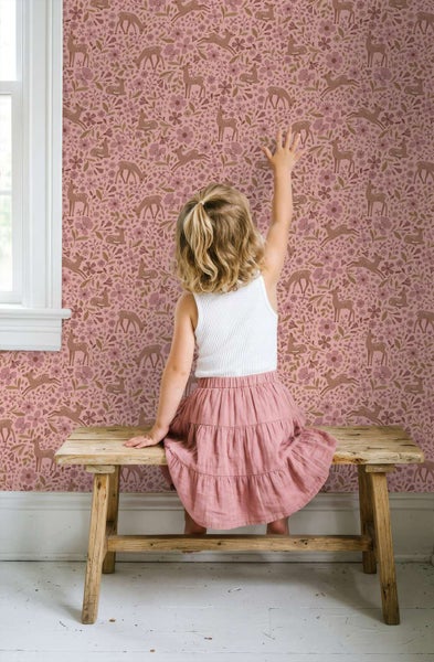 Ein Kind sitzt auf einer hölzernen Bank und berührt eine Kindertapete mit Waldmuster und Rehmotiven im Kinderzimmer.