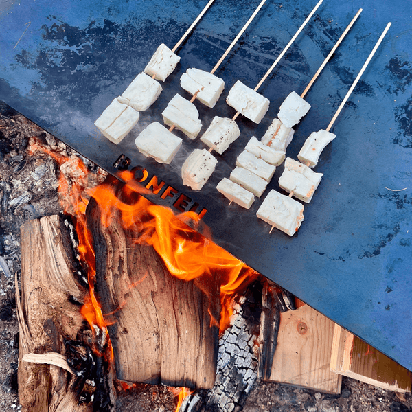 Grillspieße garen auf einer Bonfeu Grillplatte über einem offenen Holzfeuer.