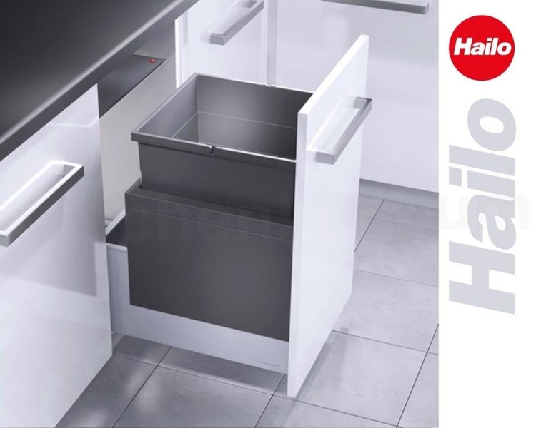 Ausziehbarer Hailo Abfallsammler in weißem Küchenschrank, dunkelgrauer Kunststoffeimer, moderne Küche mit Fliesenboden. Hailo Logo.