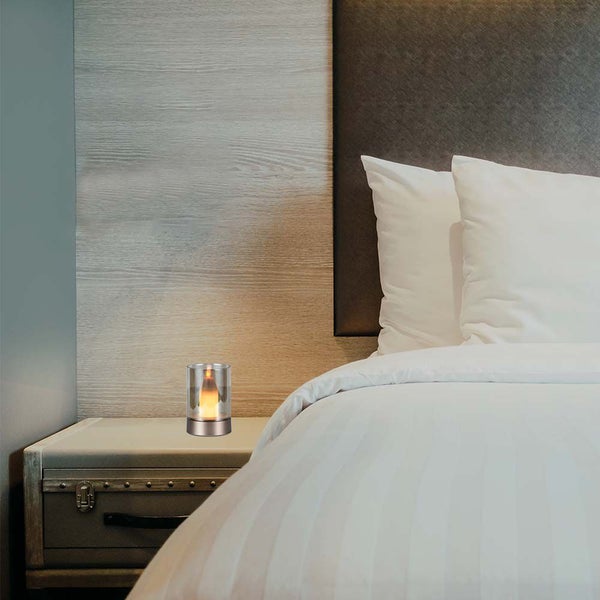 Dekorative Tischleuchte mit simulierter Flamme auf einem Nachttisch neben einem Bett.