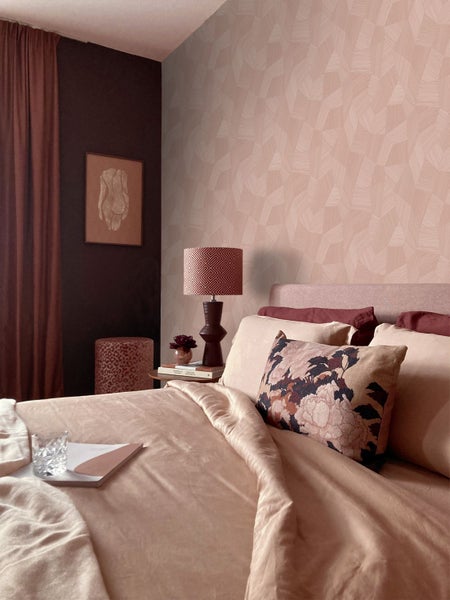 Schlafzimmer mit geometrisch gemusterter Tapete in Rosa, kombiniert mit einer dunklen Wand und farblich abgestimmter Bettwäsche.