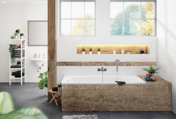 Modernes Badezimmer mit Badewanne in Natursteinoptik, Armaturen, beleuchteter Nische, Holzakzenten und weißer Wandgestaltung mit großen Fenstern.