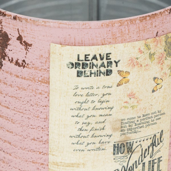 Rosafarbener Metallübertopf im Shabby-Chic-Look mit Vintage-Etikett und der Aufschrift Leave Ordinary Behind