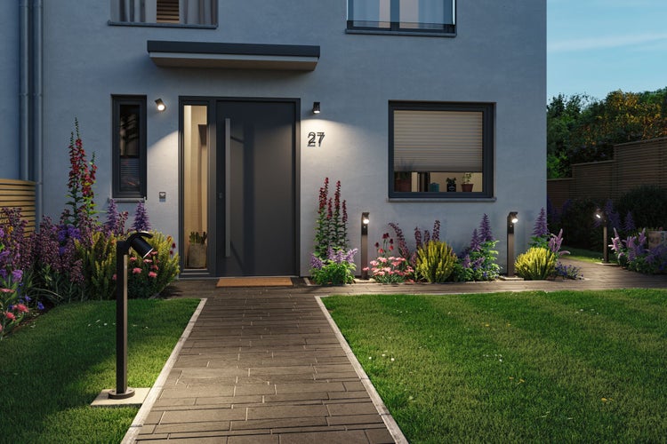 Modernes Haus mit beleuchtetem Gehweg, Außenleuchten und gepflegtem Garten mit Blumen und Rasen.