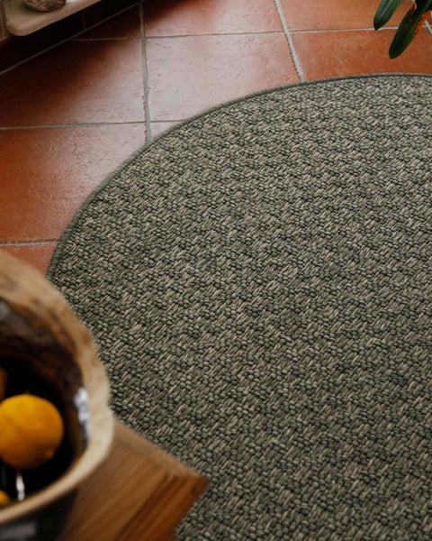 Runder, gewebter Teppich in Sisal-Optik auf einem Terrakotta-Fliesenboden.