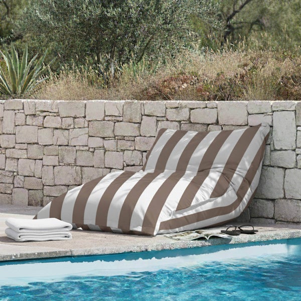 Gestreifter Outdoor-Sitzsack am Pool vor einer Steinmauer mit Handtüchern und Flip-Flops im hellen Gartenbereich.
