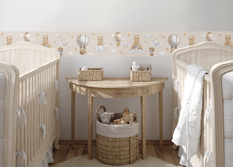 Wandbordüre für Kinderzimmer mit Motiven von Teddybären, Heißluftballons und Wolken in einem hellen Zimmer mit Gitterbetten und einem Holztisch.