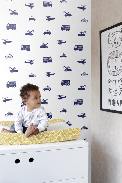 Baby auf Wickelkommode vor Wand mit Fahrzeugmotiven