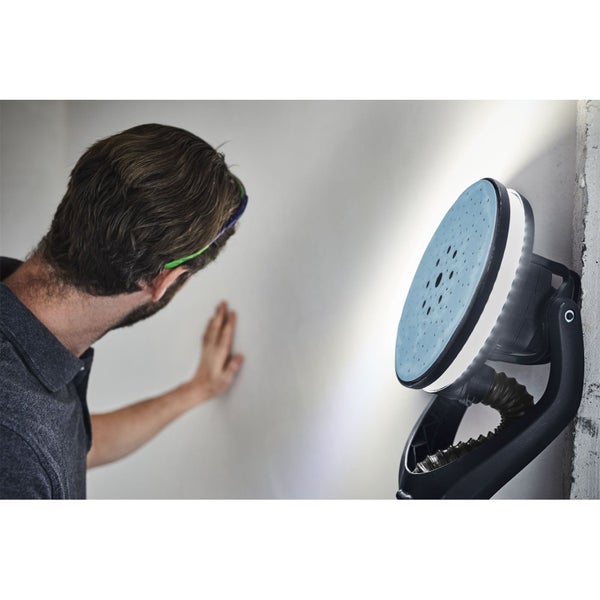 Langhalsschleifer mit integriertem LED-Lichtring beleuchtet eine Wandfläche zur Prüfung der Glätte durch einen Handwerker.