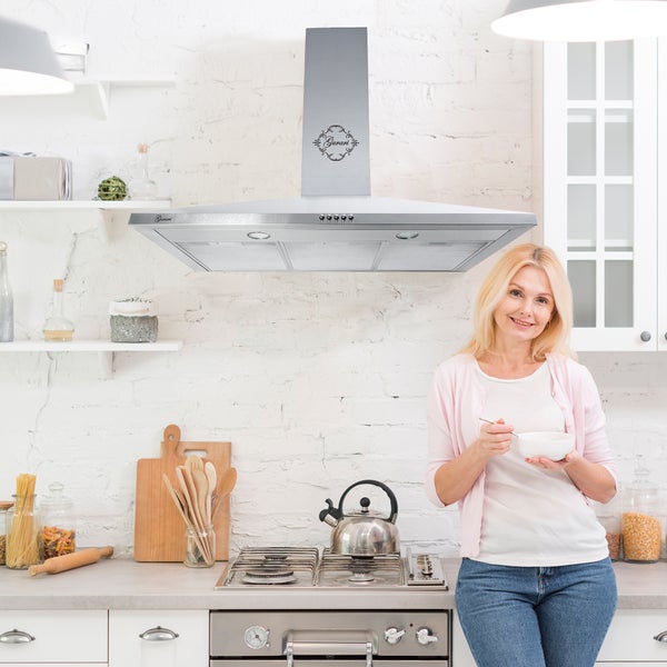 Wandhaube aus Edelstahl mit Gurari Logo über einem Gasherd in einer hellen, organisierten Küche mit weißen Ziegelwänden.