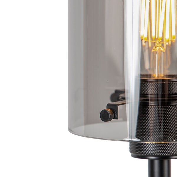 Detail einer Lampe mit zylindrischem Rauchglasschirm und sichtbarem Filament-Leuchtmittel über einem gerändelten Metallsockel.