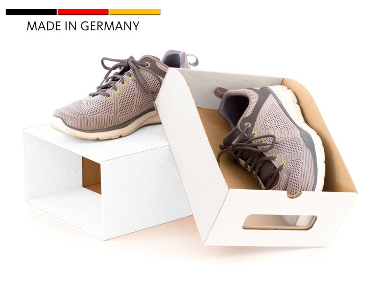 Ein Paar Sportschuhe mit Textilobermaterial in weißen Kartons mit Tragegriff, Made in Germany Qualitätssiegel.
