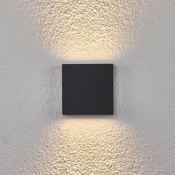 Quadratische schwarze Außenwandleuchte mit Lichtaustritt nach oben und unten auf einer strukturierten Wand.