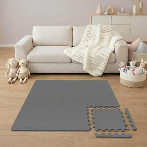 Graue Schaumstoff-Spielmatte mit Puzzlerand in einem hellen, organisierten Wohnzimmer mit Sofa und Spielzeug.