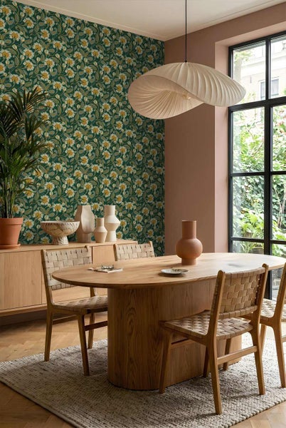 Modernes Esszimmer mit floraler Tapete, ovalem Holztisch, Geflechtstühlen und einer organisch geformten Pendelleuchte vor einem großen Fenster.