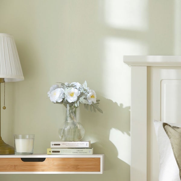 Nachttisch mit Lampe, Kerze, Blumen, Büchern und Bett im Schlafzimmer