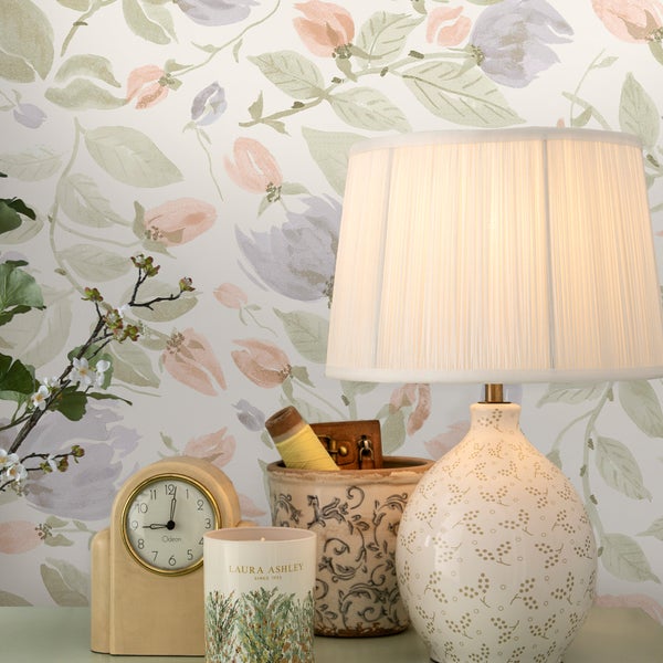 Wohnzimmer dekoriert mit einer Blumentapete mit florale Mustern und Dekorationsobjekten wie einer Tischlampe, einer Uhr und einer Duftkerze.