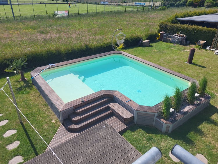 Eingelassener Swimmingpool mit einer Holzumrandung und integrierten Stufen in einem Garten mit Rasenfläche und Zierpflanzen.