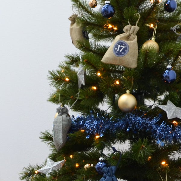 Weihnachtsbaum geschmückt mit Adventskalendersäckchen, Christbaumkugeln, Sternen und einer Lichterkette.