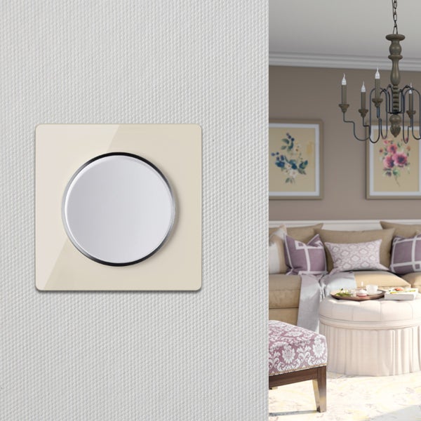 Ein moderner Lichtschalter mit rundem Drehelement auf einer strukturierten Wand, im Hintergrund ein klassisch eingerichtetes Wohnzimmer.
