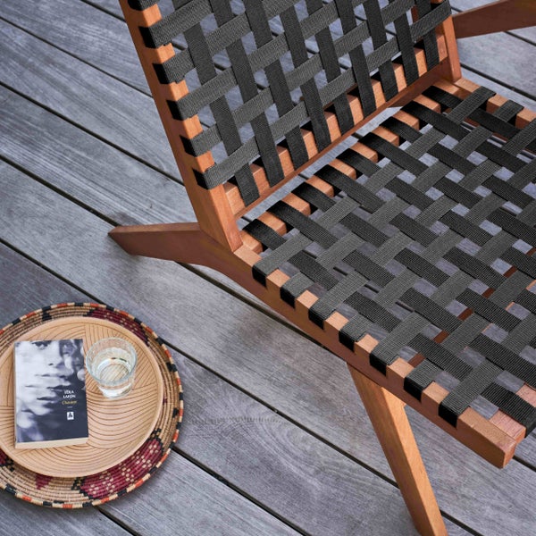 Gartenstuhl aus Holz mit schwarzer Textilbespannung auf Holzterrasse mit Dekotablett, Buch und Wasserglas.