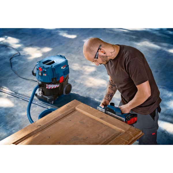 Person arbeitet mit einem Bosch Akku-Hobel an einer Holztür, angeschlossen an einen Bosch Nass- und Trockensauger.