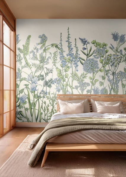 Helles Schlafzimmer mit Holzbett vor einer Fototapete mit botanischem Muster aus blauen und grünen Pflanzen und Blumen.