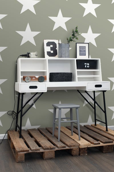 Schreibtisch mit Regalen und Stuhl auf Holzpaletten vor einer Wand mit Sternenmuster.