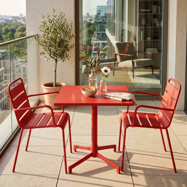 Hell gestalteter Balkon mit einem roten quadratischen Metalltisch, zwei Gartenstühlen und einem Olivenbaum im Topf neben einem Glasgeländer.