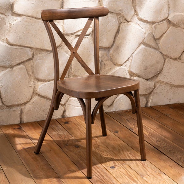 Brauner Bistrostuhl aus Holz mit Kreuzrückenlehne auf einer hellen Holzterrasse vor einer rustikalen Steinwand.