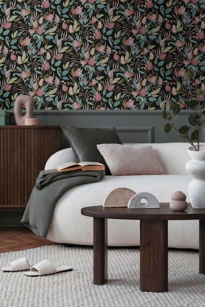 Wohnzimmer mit Vliestapete mit Blumenmuster, weißem Sofa, Holztisch und dekorativen Accessoires in einer modernen und gemütlichen Einrichtung.