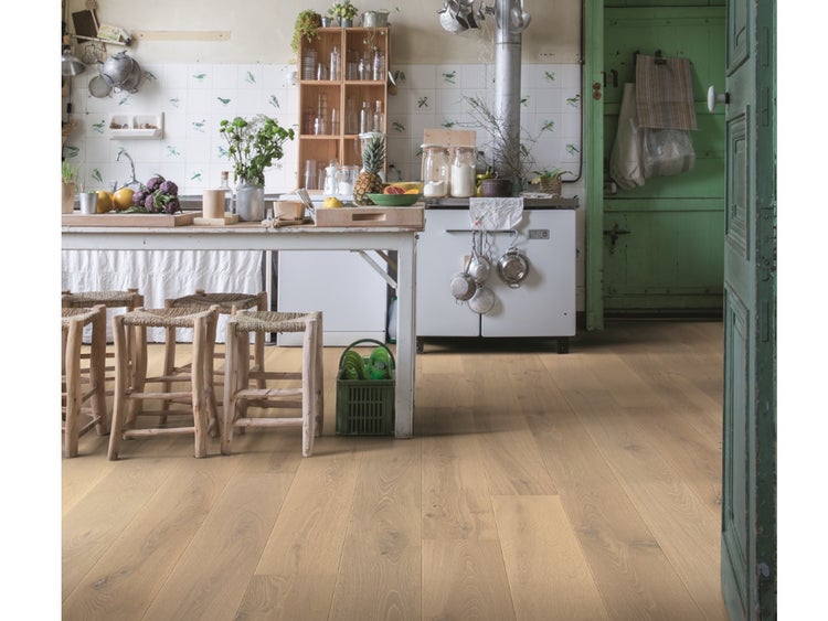 Helle Küche mit rustikalem Parkettboden aus Eichenholz, weißem Holztisch mit geflochtenen Hockern und nostalgischer Einrichtung.