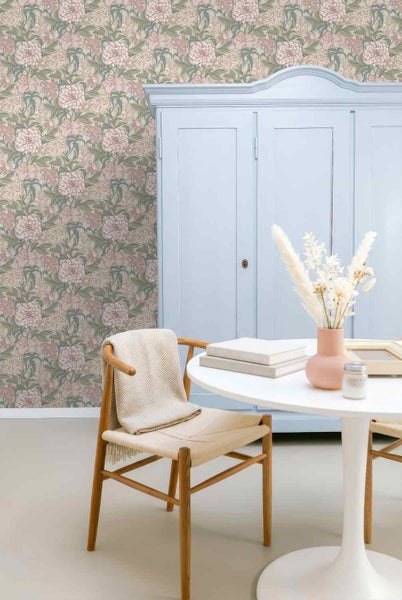 Vliestapete mit floralem Pfingstrosen-Muster in einem hellen Zimmer mit Schrank, Tisch und Holzstuhl.