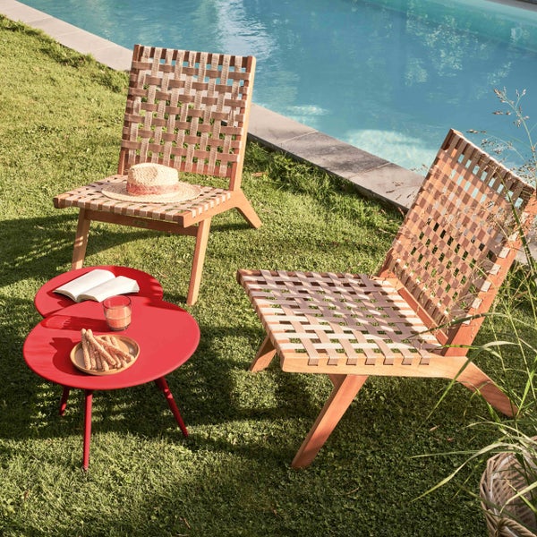Zwei Gartensessel aus Holz mit Geflecht und ein kleiner runder Beistelltisch auf Rasen neben einem Pool.
