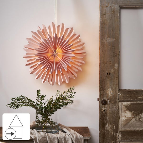 Dekorative Papiersternlampe hängt an der Wand, kombiniert mit einer Vase mit Zweigen auf einem Holztisch neben einer alten Tür.