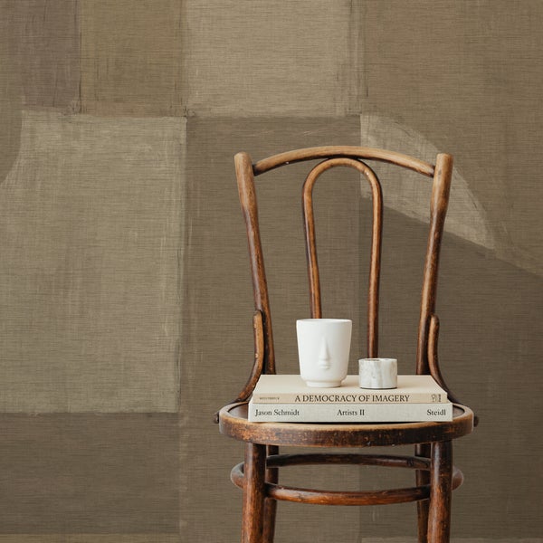 Dekorative Wand mit abstraktem Muster hinter einem Holzstuhl mit Büchern, einer Tasse und einer Kerze