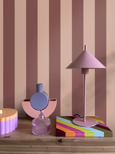 Moderne Raumgestaltung mit vertikal gestreifter Tapete, Sideboard aus Holz, Tischleuchte aus Metall und dekorativen Wohnaccessoires.